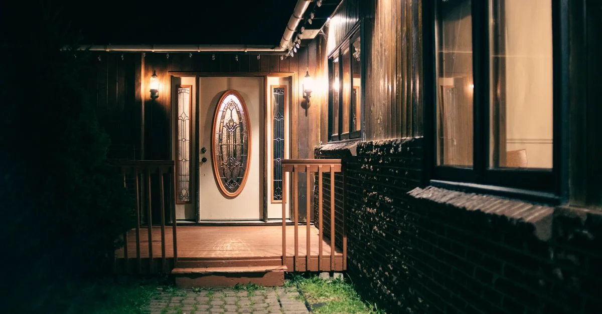 Une entrée de maison chaleureusement éclairée avec des portes en verre décoratives et des lanternes lumineuses la nuit.