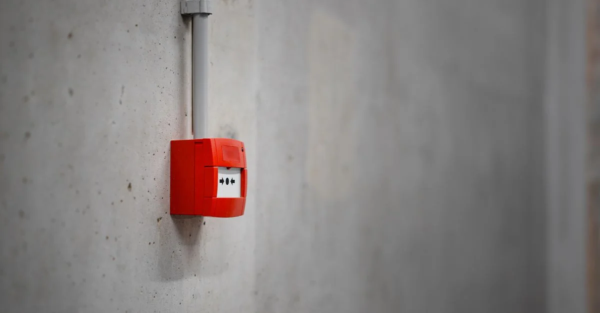 Une boîte d'alarme rouge montée sur un mur en béton gris, offrant une sécurité urbaine.