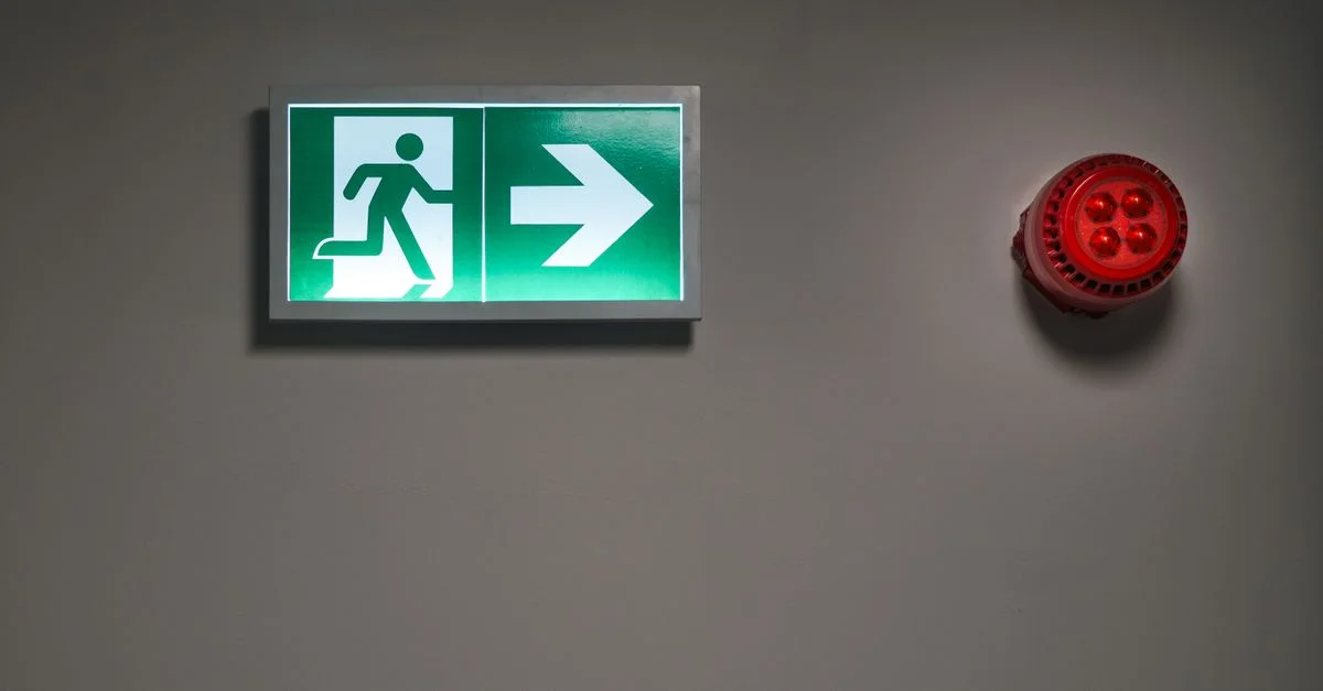 Un panneau de sortie de secours lumineux et une alarme dans un couloir intérieur indiquent la voie d'évacuation d'urgence.