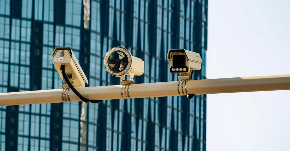 Caméras de surveillance montées sur un poteau devant un bâtiment moderne en verre.