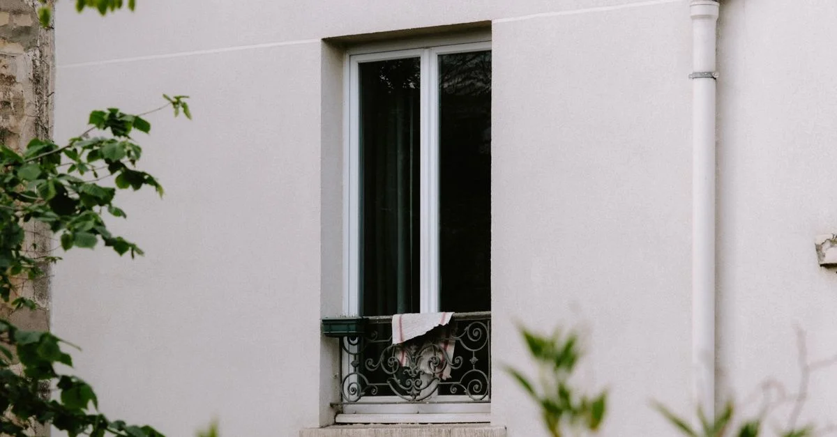 Une fenêtre avec une grille décorative et un tissu sur le mur d'un bâtiment résidentiel.