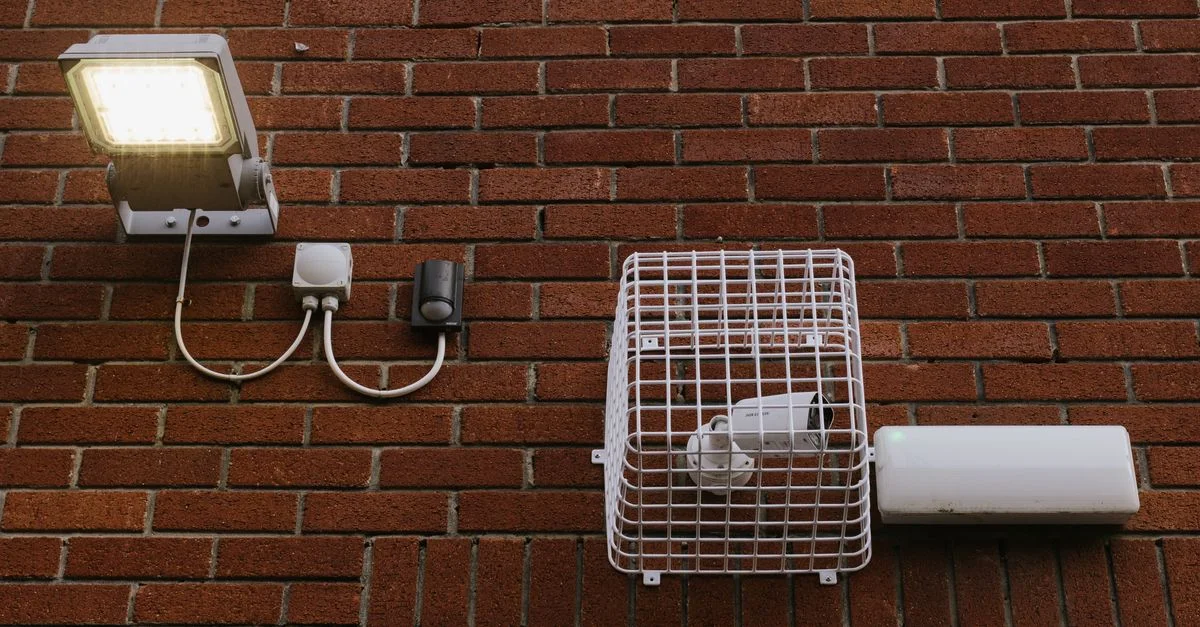 Vue rapprochée d'un mur en briques avec une lumière LED et une caméra de sécurité en cage.